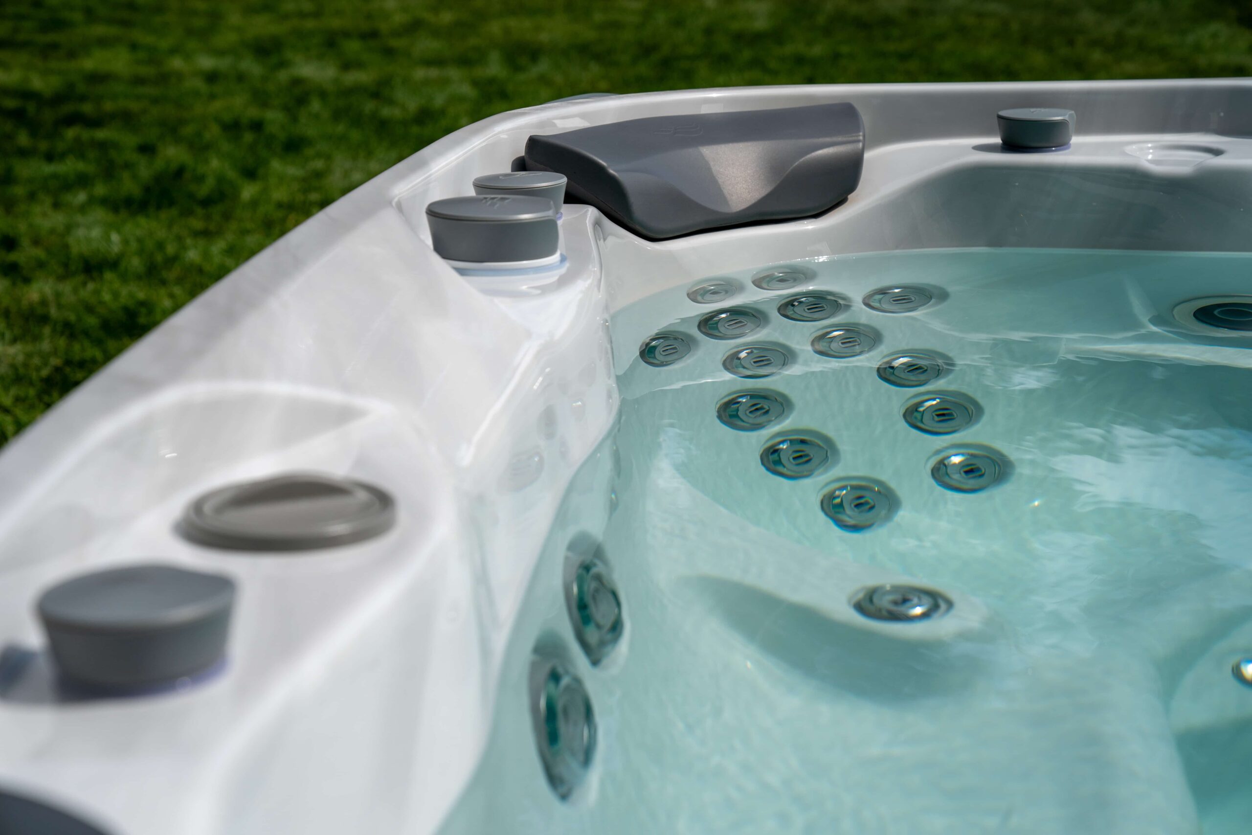 Up close image of clear blue water of a hot tub at a Newtown, CT home. Jets are off, water is still. Green grass can be seen blurred in the background in the upper left corner.